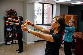 Homg Miller leads a fitness class for in person participants at the Detroit office of the Association of Chinese Americans and participants on Zoom.