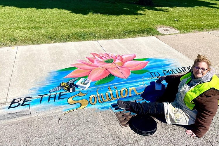 Local artist Donna Mitchell-Collins poses with one of her storm drain murals in downtown St. Clair, Michigan.