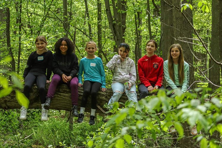 Some of Nikki DeGowske’s 5th-grade students sitting on a fallen tree at their outdoor classroom at Algonquin Elementary School.