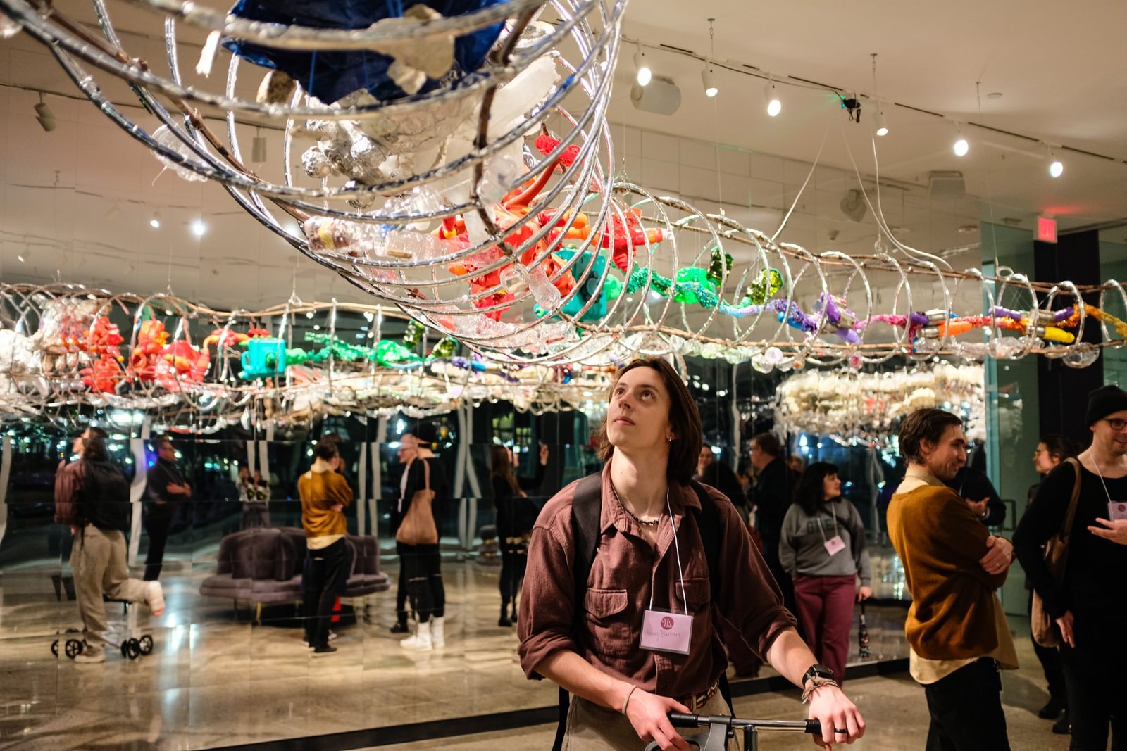 A participant in the University of Michigan Museum of Art's Queer Night stands under artist Machine Dazzle's "Ouroboros" sculpture.