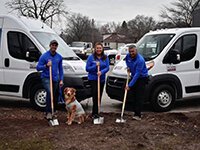 Thomas Howell (left), Vanessa Howell, and William Howell stand with Apcom's mascot Brady posing with shovels indicating the start of the new Apcom.