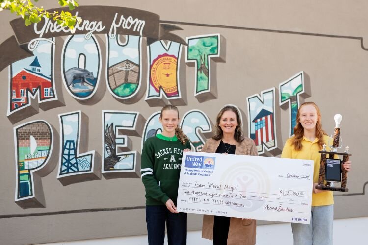 Olivia Harding (left), United Way’s Annie Sanders (middle), and Claire Campbell (right) pose in front of the new mural in downtown Mt. Pleasant.