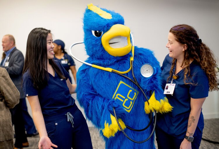 MCC students Kaili Prins, left, and Marissa Aney-Johnson joke with Muskegon Community College mascot Jay the Jayhawk. The two students spoke during the event.