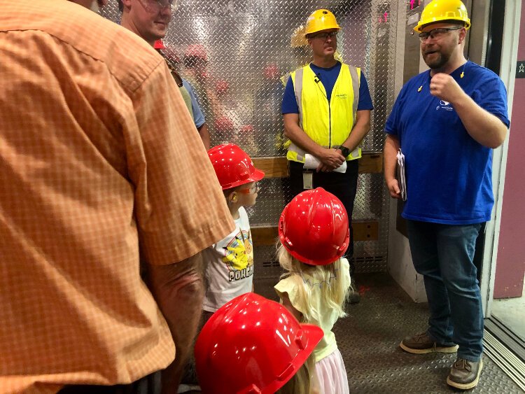 Nate Hoffman (right) and Norm Kapla (center) welcome guests onto an elevator at the J.H. Campbell Complex Unit 3 power generating station at Port Sheldon Township. Two hundred and fifty people registered rare public tour of the facility.