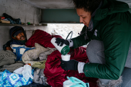 Madison Williams pours hot chocolate for Loy McDowell, who lives under a pedestrian bridge next to I-75