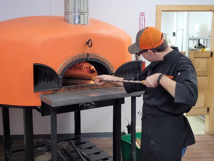 Jameson Baker places a pizza in the oven.