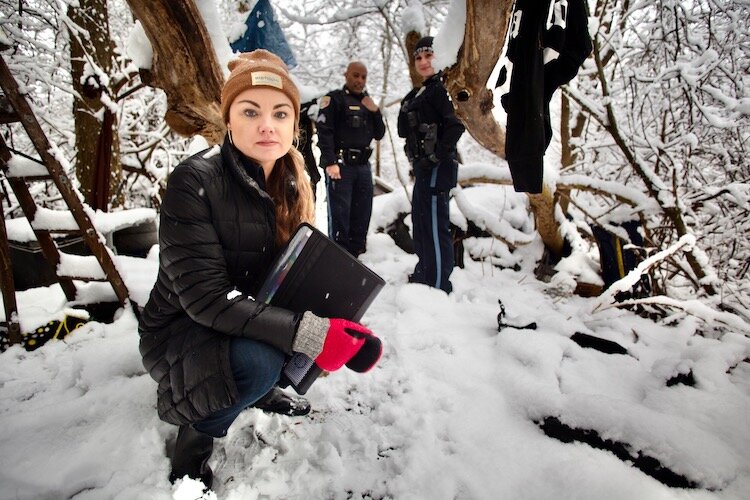 Kelsey Harness, social services coordinator for Kalamazoo Public Safety's new Community Service Team, looks around a wooded area where unhoused people  camped until recently on the city's East Side.