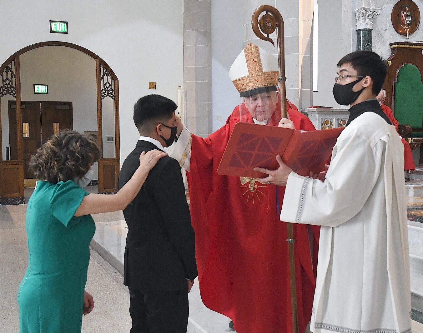 Bishop Paul Bradley of the Catholic Diocese of Kalamazoo, wearing protective gear, confers the sacrament of Confirmation at St. Augustine Cathedral last year.