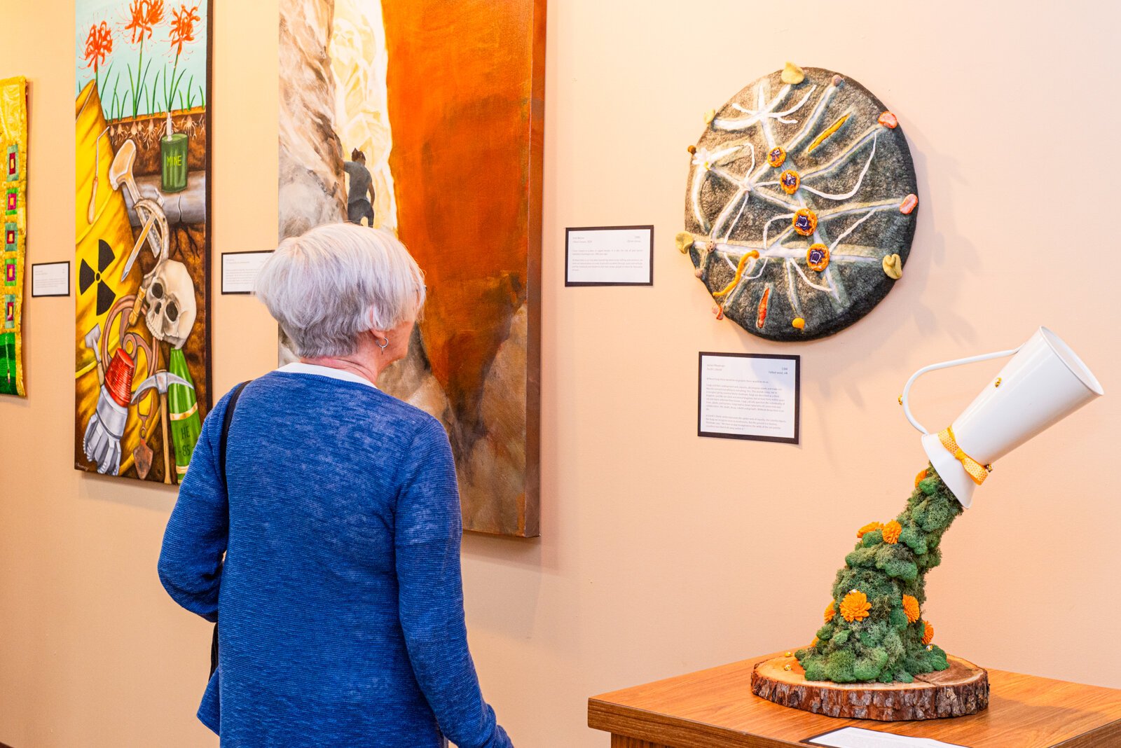 Patron Admiring Janice Maatman's piece "Earth's Shield" next to Stephanie Diep's piece "A Land Flowing with Dandelions."