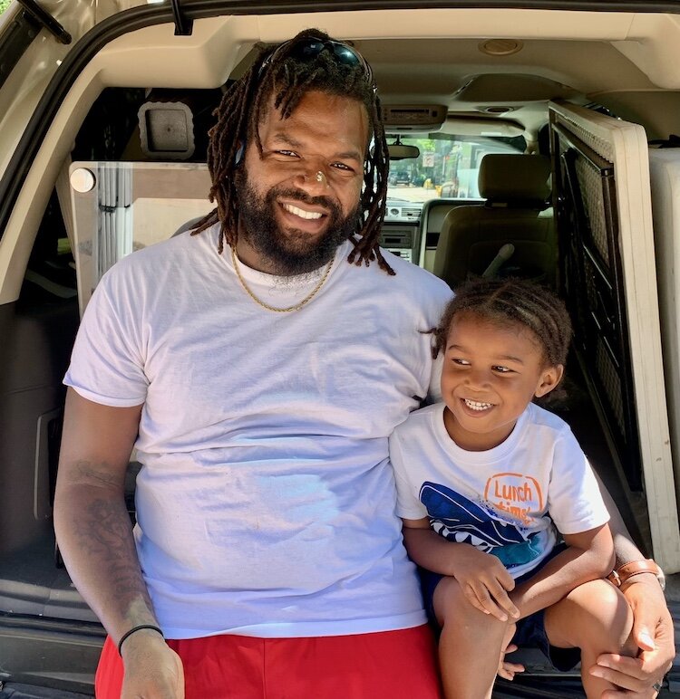 DeMargeo White and his son, Roman, 4, take a break on Thursday, June 6, 2024, from unloading products for White’s business Huey D’s Goodies.