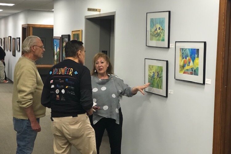 Carol Bueno, an artist and member of LAGL, talks with visitors who came to see an exhibit of LAGL's work at Commerce Pointe.