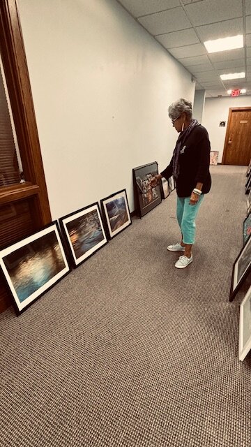 Framed work from some of the 28 artists who will be part of the exhibit, are carefully placed against the walls of the Commerce Point Gallery by Linda Tafolla, Curator of the space.