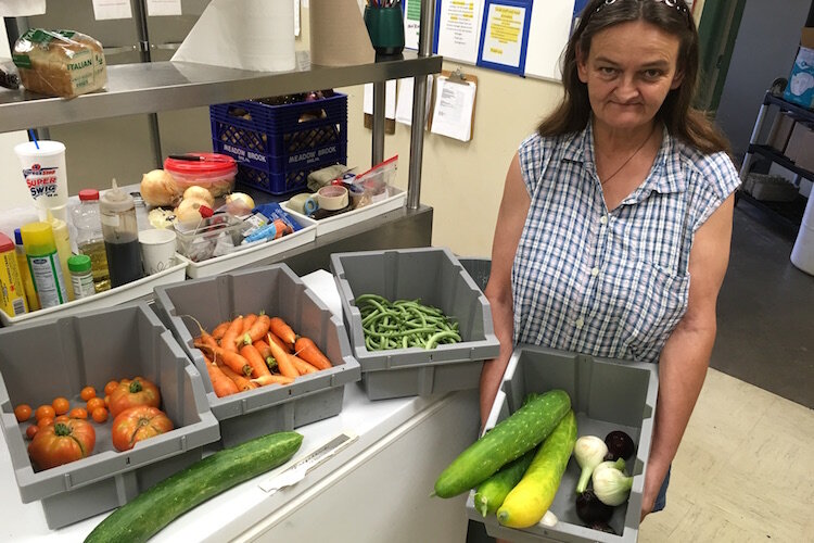 Linda, a consumer of the SHARE Center, stands in the organization's kitchen and holds a bowl containing some of the vegetables grown in the garden.