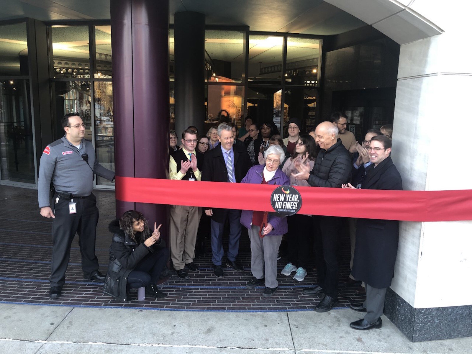 Lisa Godfrey, president of the Kalamazoo Public Library Board of Directors, center, cuts a ribbon declaring the library a fines free library on January 2, 2020, flanked to left by library director Ryan Wieber and Kalamazoo Mayor David Anderson, right