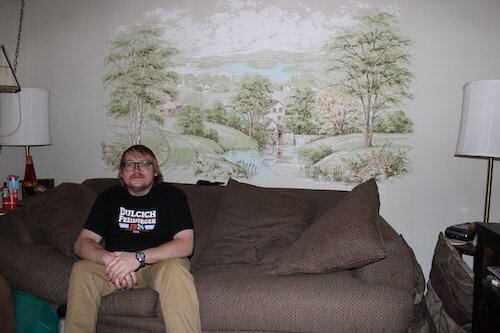 Thomas Kuehn relaxes in his Three Rivers living room. The house on South Constantine Street came with the wall art