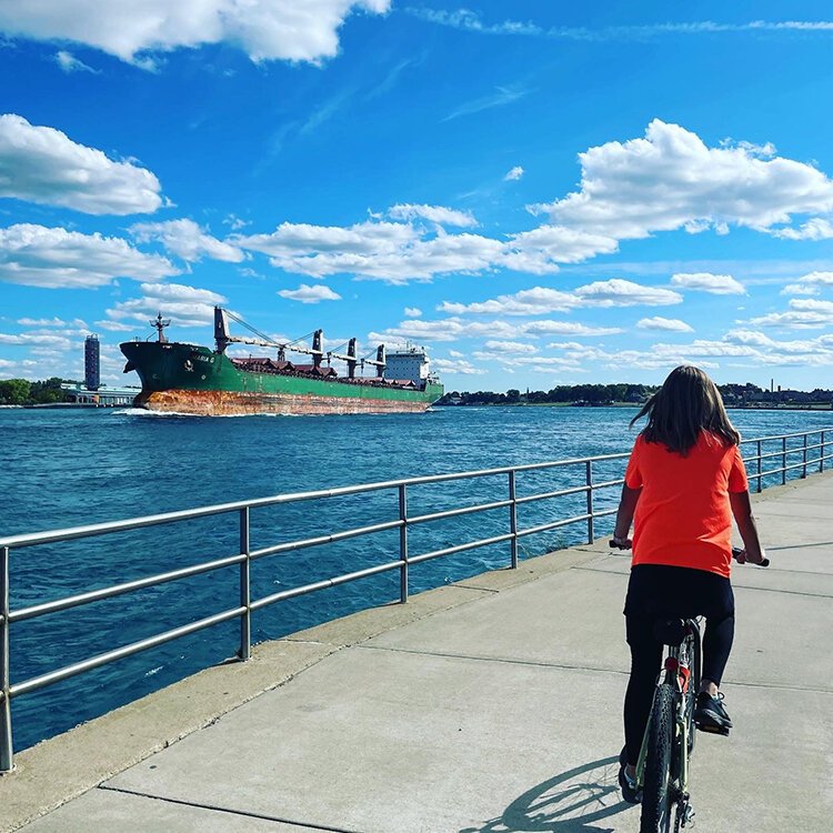 A resident riding along the Bridge to Bay trail with a freighter out on the lake.