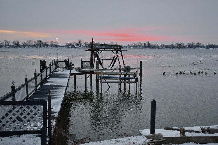 The St. Clair River flowing under a snow-brushed wooden pier at dawn.